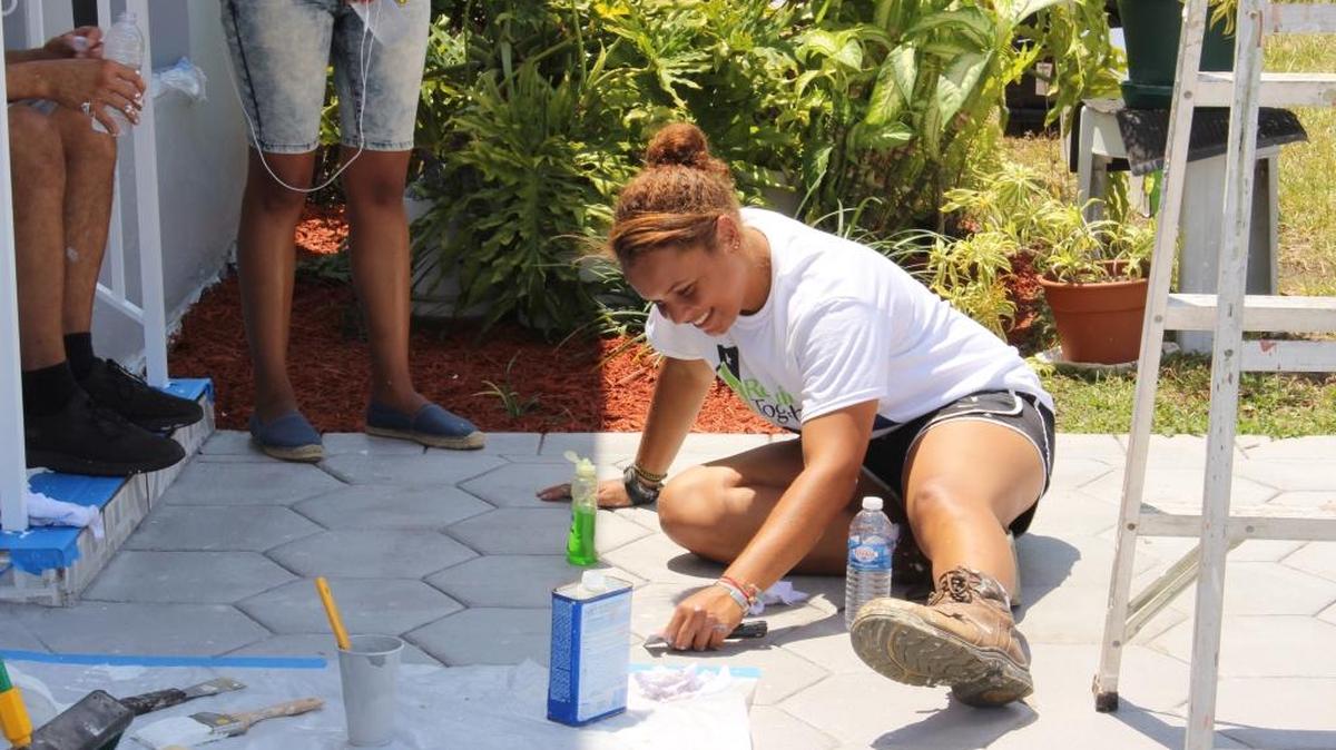 Sydney Turner, 23, Americorps project coordinator for Rebuilding Together, cleans up as she scrapes the paint off the concrete floor of the parkinglot in the Smith residence