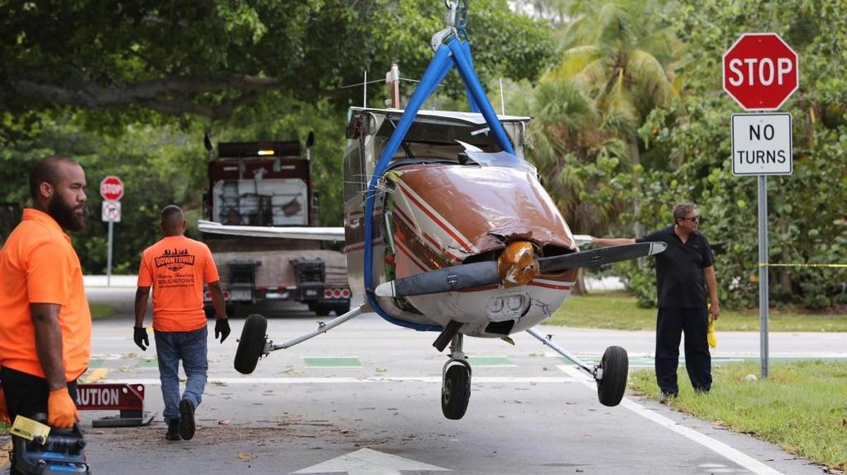 A worker prepares to remove small plane that sits on a road Friday, July 14, 2017, in Key Biscayne, Fla. The pilot and a student, on a training flight late Thursday, walked away after crash landing on the road.