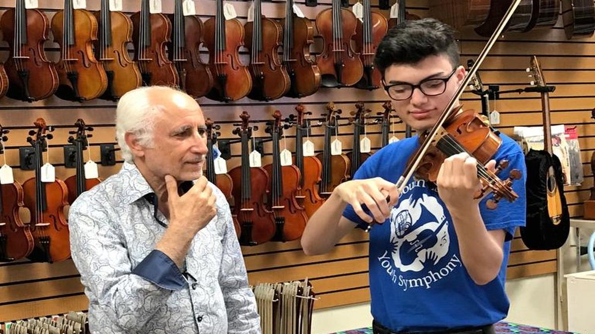 Manuel Berberian, left, owner of Allegro Music Center, listens to Yosvani Rodriguez, 16, play a violin he donated to him.