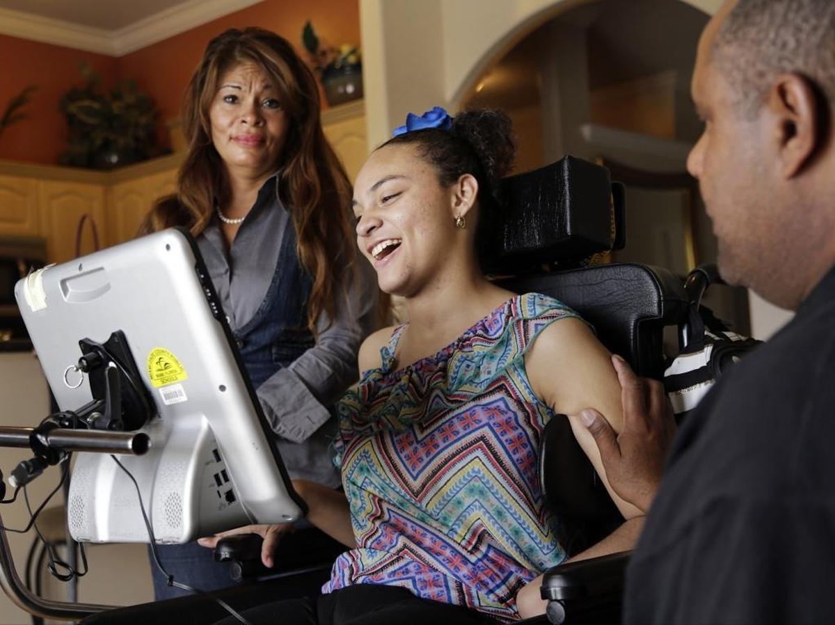 Angelyn Gutierrez (center) can’t speak, but she has learned to communicate through a computer. Here she laughs in her West Kendall home as her parents Aida, left, and Flavio, right, look on.