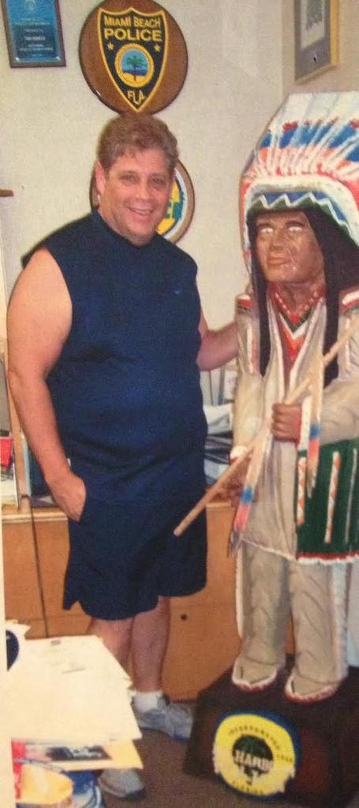 A photo of Tom Hunker and the wooden Indian, carved in his likeness, that adorned his office at the Bal Habour police station. 