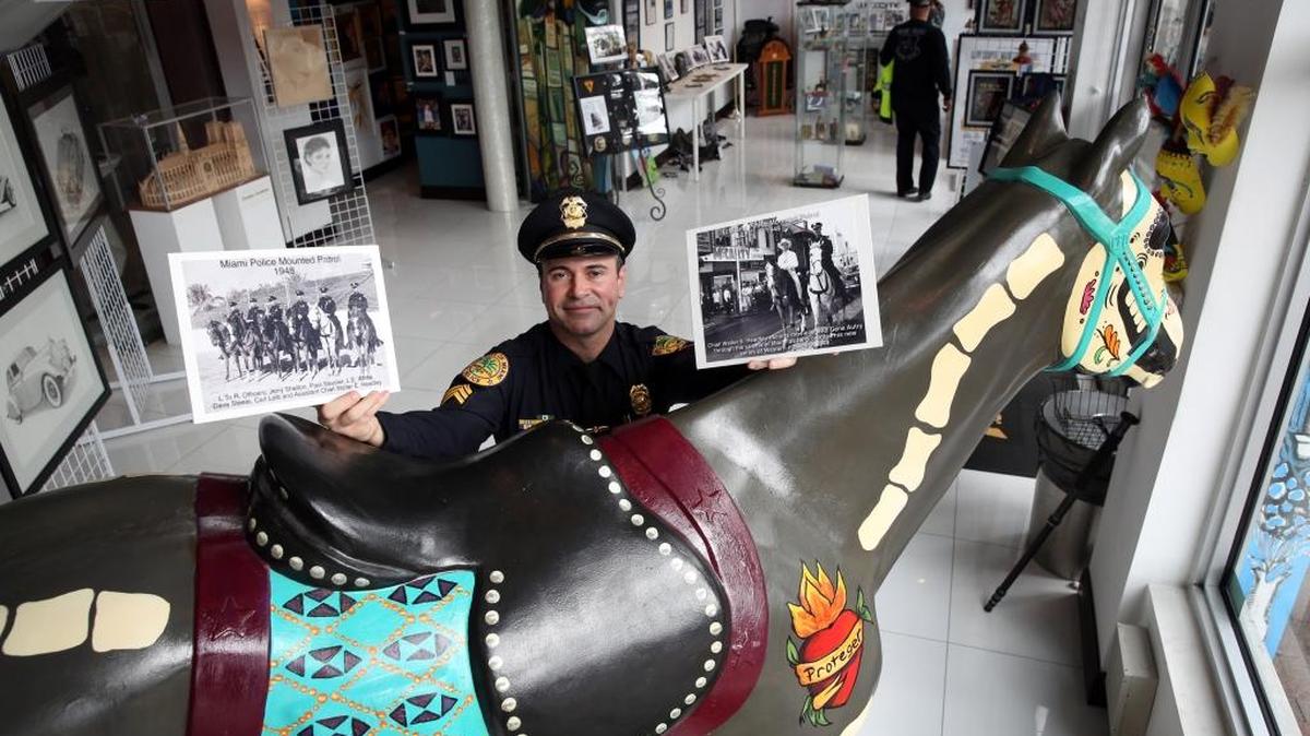 Miami Police Sgt. Eddie Perez shows some past mounted police photos while standing by Diego, a life-size Horse of Honor sculpture, at The Futurama Art Gallery on Jan. 27, 2016.