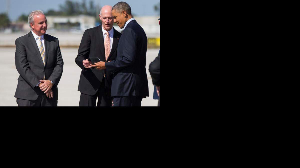 
Miami-Dade County Mayor Carlos Gimenez watches at left as Florida Gov. Rick Scott gives a Miami Marlins baseball cap to President Barack Obama upon the president's arrived at Miami International Airport on Wednesday. 
