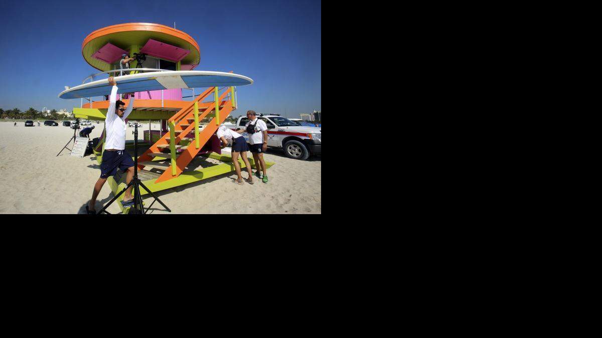 
Miami Beach Lifeguard/EMT Jason Casanova carries a rescue paddle board past his new work station on Friday, March 20, 2015, after a ribbon-cutting ceremony at which Miami Beach officials unveiled one of the city's two new lifeguard towers. This brightly-colored structure is on the beach at 10th Street, behind Ocean Rescue headquarters. Casanova and fellow lifeguard/EMT Cayetano Garcia will team up at this post to keep beachgoers safe. The new towers are added to the already-iconic 29-piece collection between South Pointe and 87th Street. The new round tower's color scheme is ice plant green, fusion pink and knockout orange.
