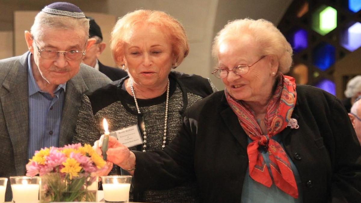 Holocaust survivors Joe Birnbaum, left, and Bessie Beszow, center, light candles with some help during an interfaith community gathering in response to the rise anti-semitism and hate inside Temple Beth Sholom on Holocaust Remembrance Day.