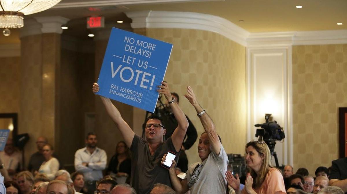 People hold signs during a Bal Harbour Village Council meeting Wednesday.