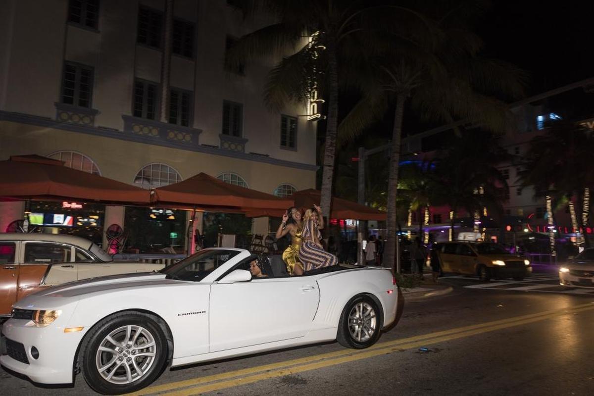 Two women ride in the back of a convertible as it drives along Ocean Drive.
