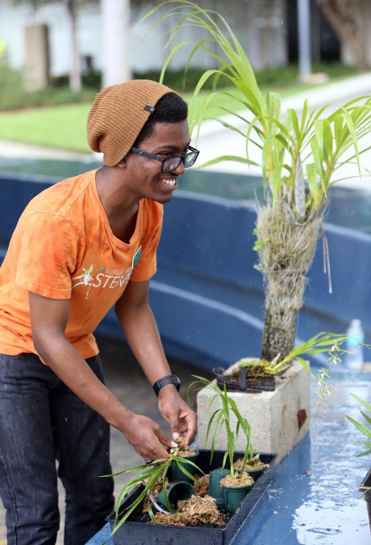 Myles Covington, a student volunteer with Fairchild Gardens, is all smiles while working with the orchids, even as the rain pours down Friday during a ceremonial orchid planting at Miami Beach City Hall.