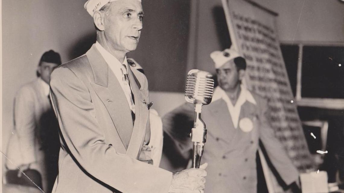 Circa 1955: Caesar La Monaca holds a microphone, with Miami Sheriff Thomas Kelly in the background.