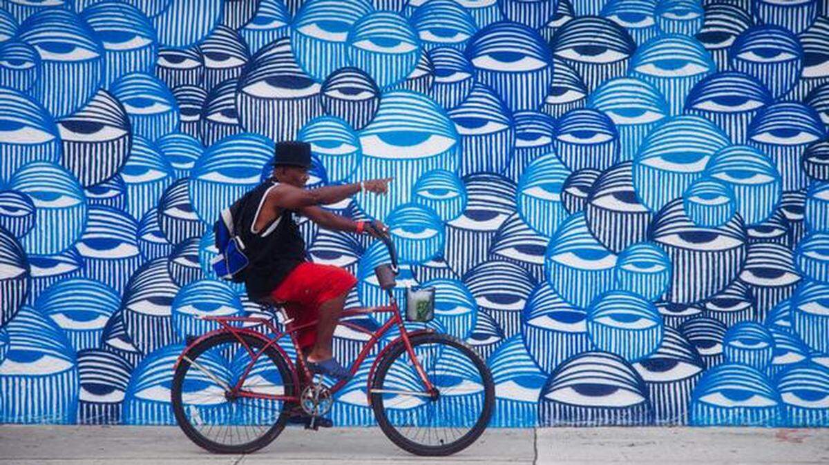 
A man rides his bike on the sidewalk in front of a mural painted by artist Ahol Sniffs Glue in Wynwood. 
