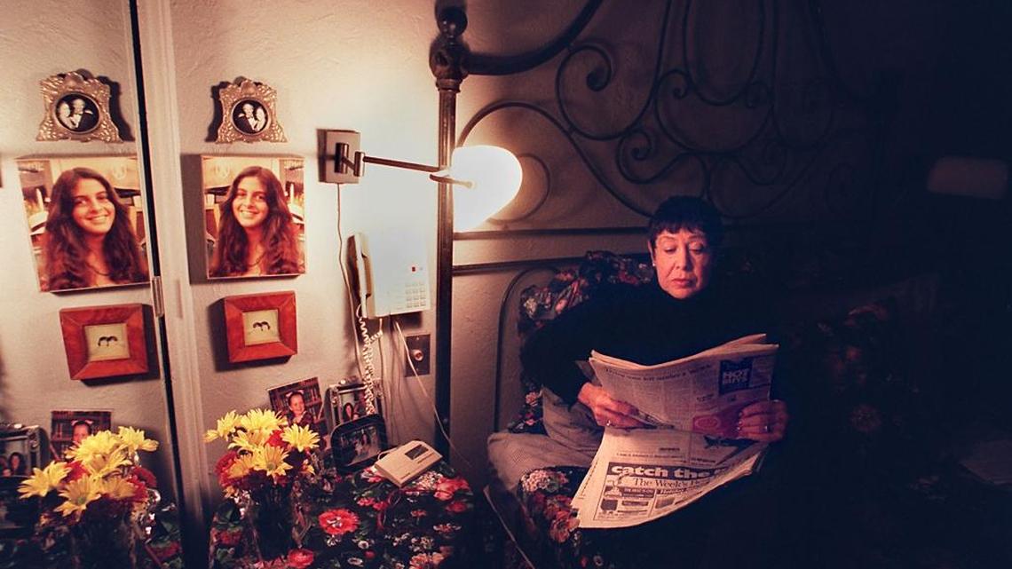 Sue Billig reads the paper in her bedroom near a photo of her daughter Amy and the telephone.