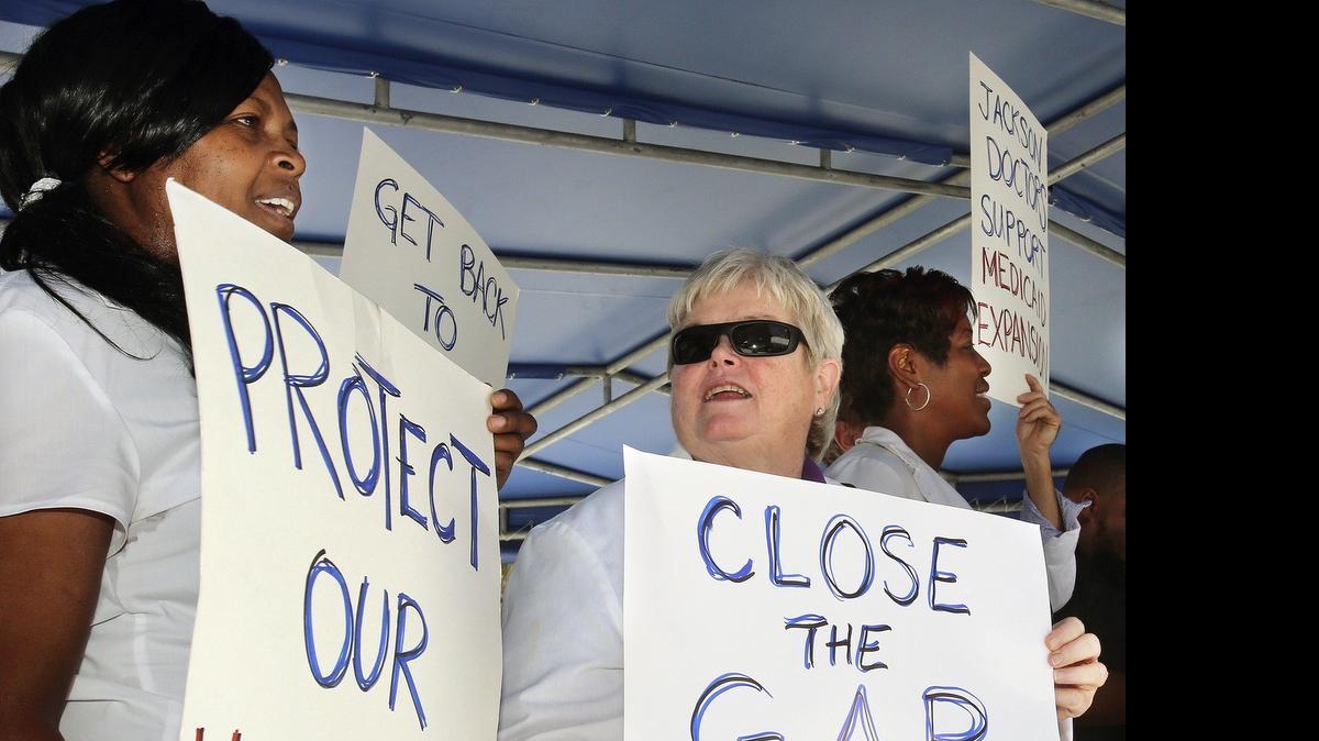 
Longtime Jackson Health System registered nurses Lisa Ward, left, and Barbara Scollon, center, hold hand-lettered signs during a press conference and rally supporting Medicaid expansion, on Friday, May 8, 2015 on the main Jackson campus in Miami. 
