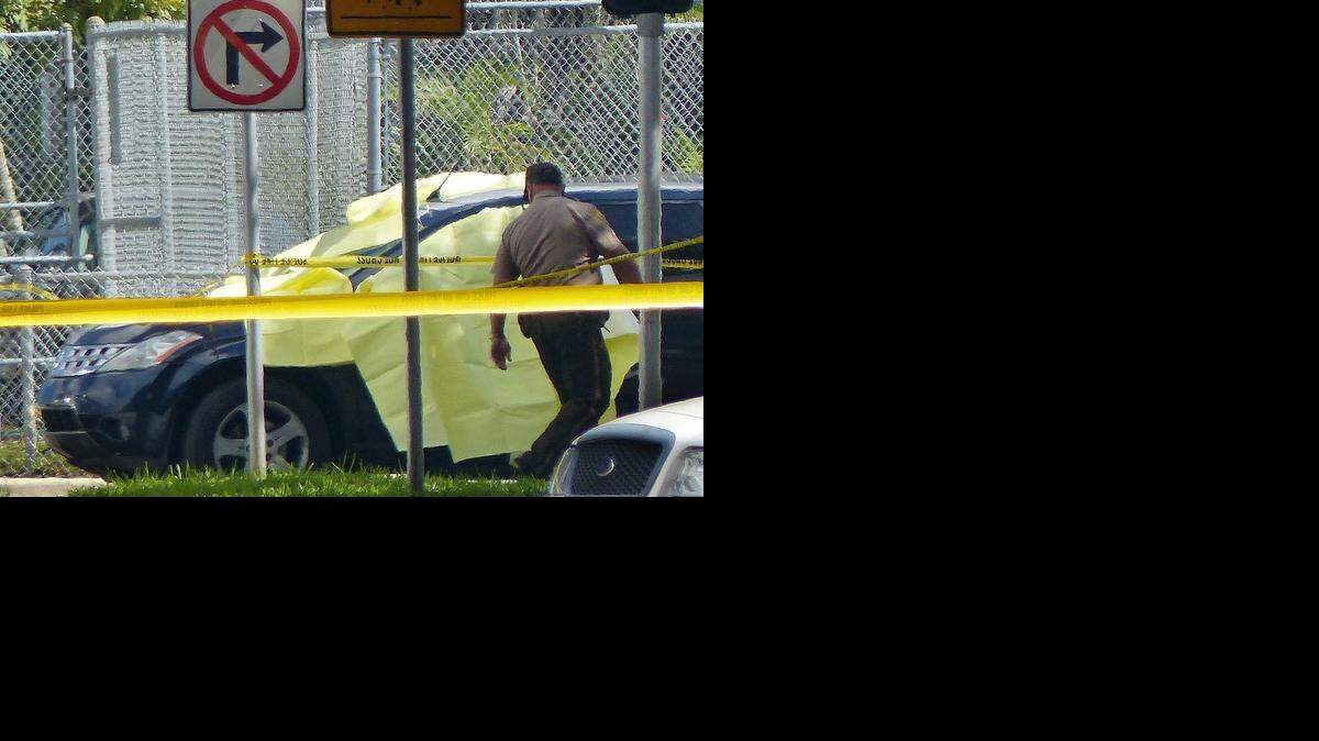 
A police officer inspects a car covered with a yellow tarp where the body of a suspected bank robber lies after an exchange of gunfire with police on Monday across the street from Biscayne Gardens Elementary School on Monday, Nov. 3, 2014.
