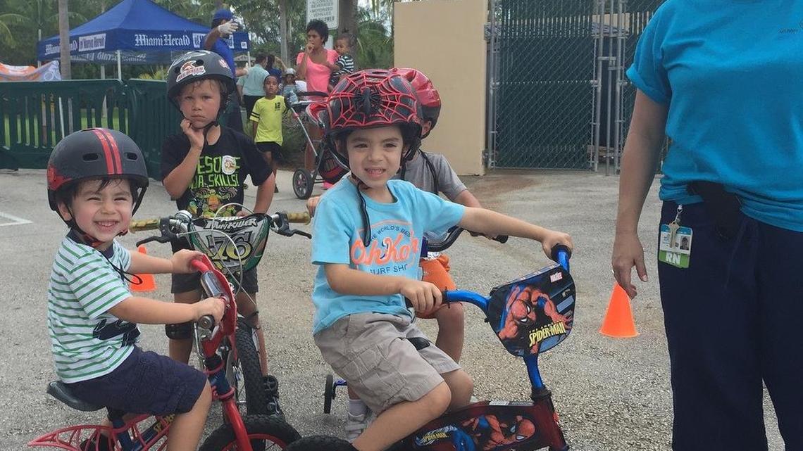 
James Cisneroz, 3, and Phillip Cisneroz, 5, forefront, as they await to participate in the bicycle rodeo after having their helmets fitted. They’re standing next to Malvina Duncan, RN, an injury prevention program coordinator with Nicklaus Children’s Hospital, and the Safe Kids coordinator for Miami-Dade County.
