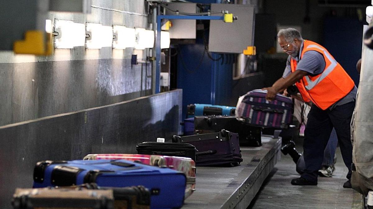 In this 2013 file photo, a baggage handler unloads luggage from an incoming flight at Miami International Airport.