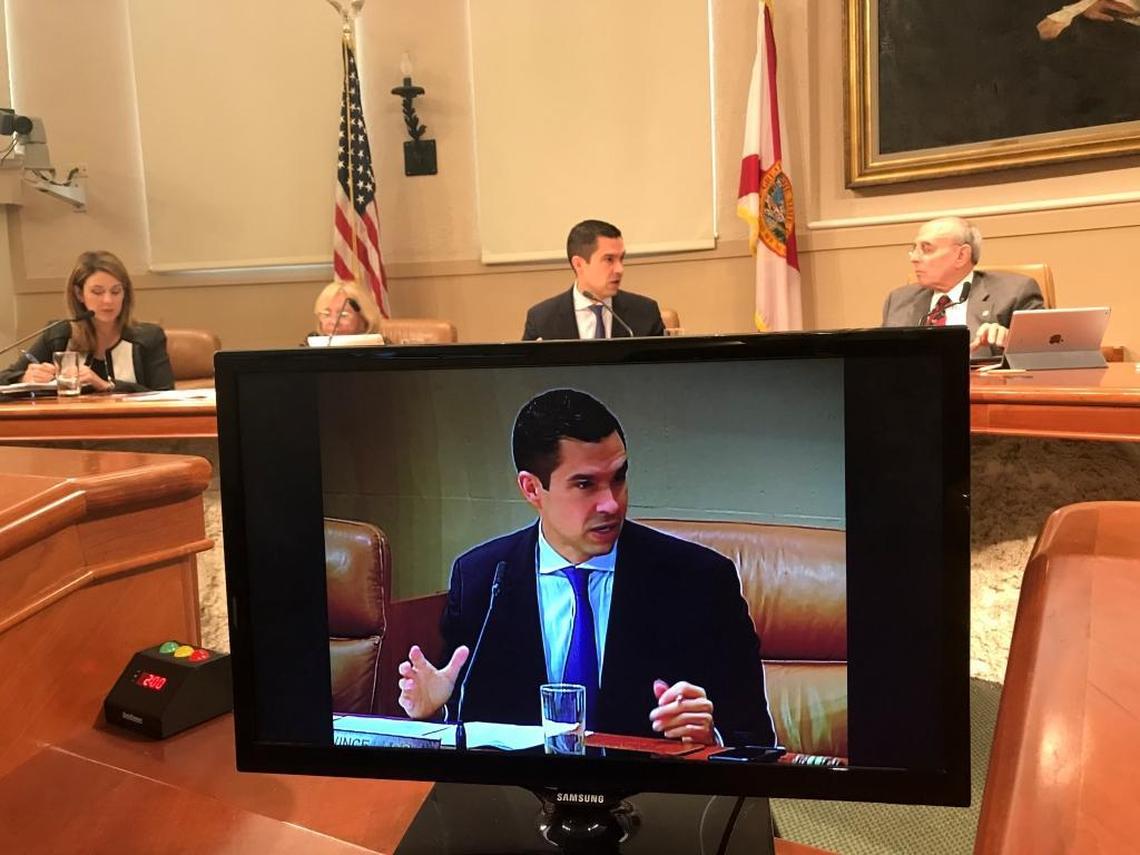 Coral Gables City Commissioner Vince Lago speaks during the March 20, 2018, commission meeting, where a proposed local ban on the sale of assault rifles was defeated. Lago, pictured on one of the video screens broadcasting the action to spectators at City Hall, cast one of the three No votes. To his left on the dais is the ban’s sponsor, Mayor Raúl Valdés-Fauli; to his right is Commissioner Patricia Keon. To Keon’s right is City Attorney Miriam Soler Ramos.
