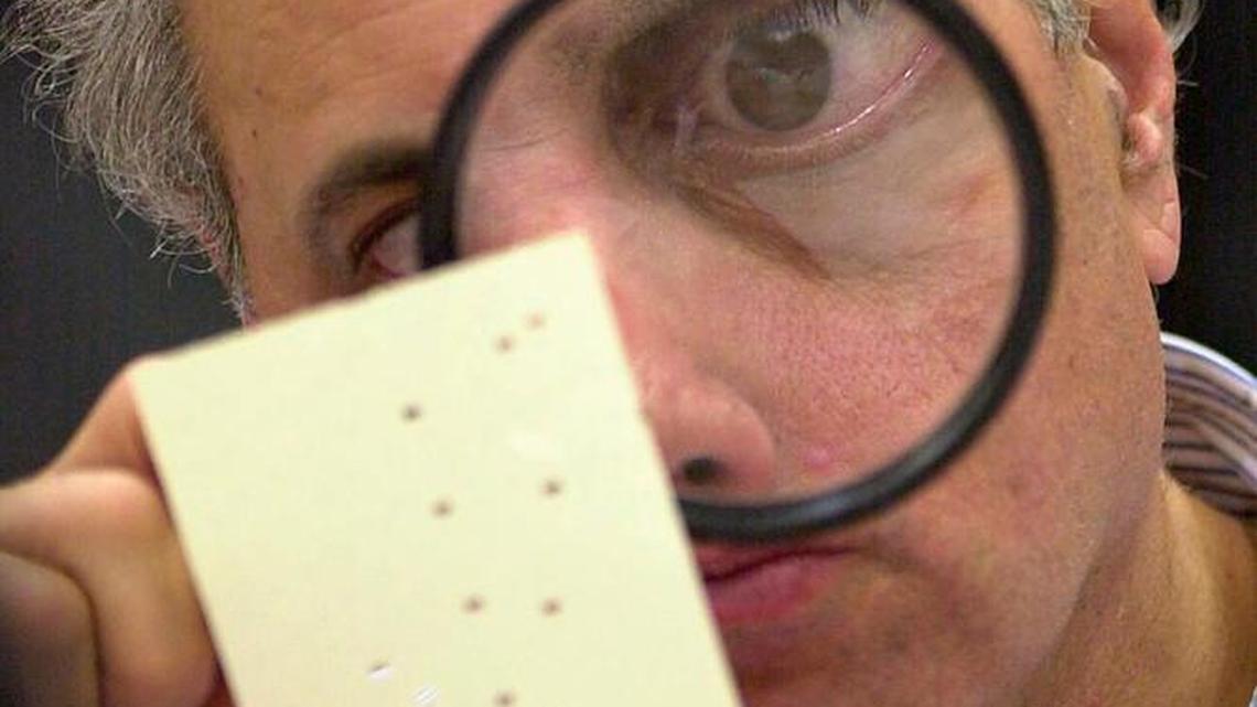 In this file photo, Broward County canvassing board member Judge Robert Rosenberg uses a magnifying glass to examine a disputed 2000 presidential election ballot at the Broward County Courthouse