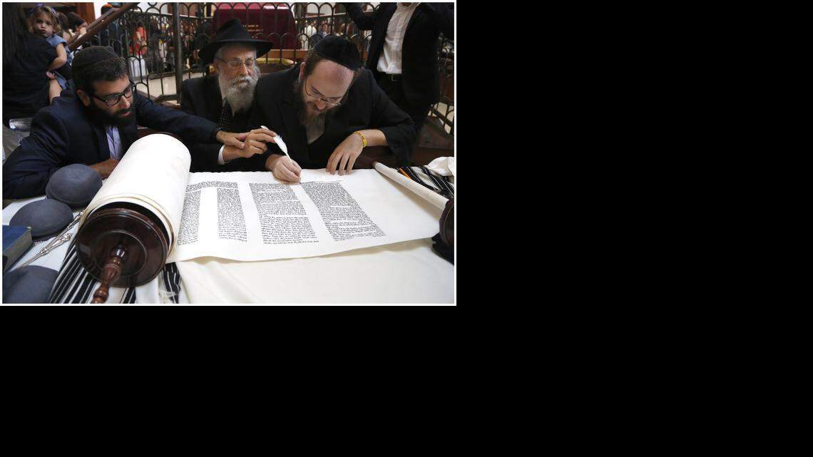 
Rabbi Zalman Lipskar, left, and his father, Rabbi Sholom Lipskar, place their hands on the feather pen of the scribe Yochanan Klein as he writes on the Torah. The Lipskars are rabbis at The Shul in Surfside. His son joined the congregation about 10 years ago, after working in the business world. On Sunday, September 21, 2014, the pair attended a Torah dedication ceremony at The Shul.
