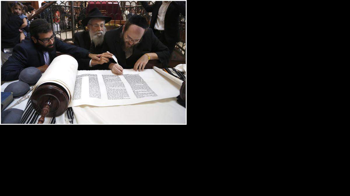 
Rabbi Zalman Lipskar, left, and his father, Rabbi Sholom Lipskar, place their hands on the feather pen of the scribe Yochanan Klein as he writes on the Torah. The Lipskars are rabbis at The Shul in Surfside. His son joined the congregation about 10 years ago, after working in the business world. On Sunday, September 21, 2014, the pair attended a Torah dedication ceremony at The Shul.

