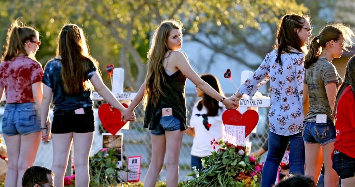 Mourners stand near a cross at Marjory Stoneman Douglas High School in the wake of a shooting massacre that left 17 people dead. The mass shooting, like others before it, unleashed a local and national debate on gun control.