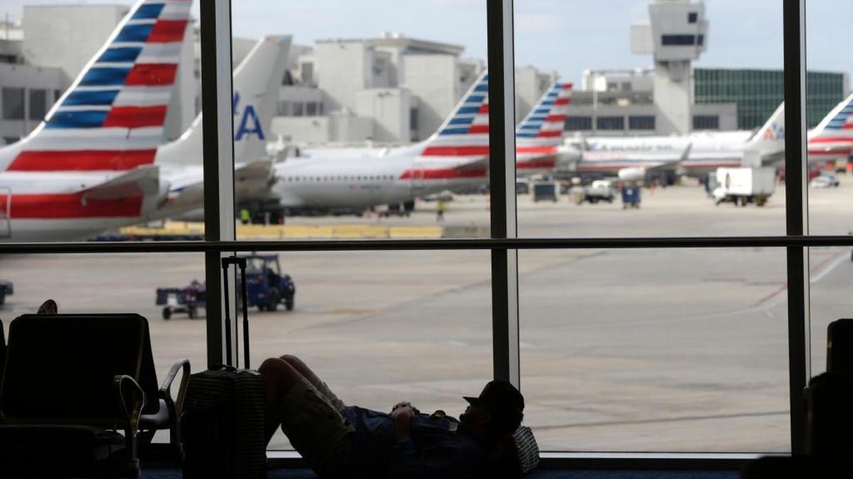 A traveler rests on the floor as American Airlines aircraft are lined up the the gates at Miami International Airport on Tuesday, Nov. 24.