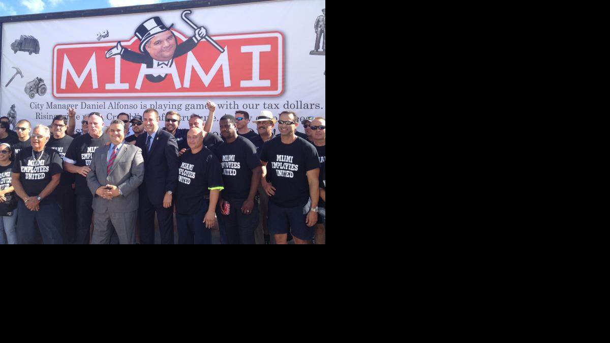 
Miami City Manager Daniel Alfonso (middle) poses for a picture next to FOP president Sgt. Javier Ortiz before Miami’s first budget hearing in September. The city and union now have a tentative contract. The billboard in the back portrays Alfonso as Monopoly’s Rich Uncle Pennybags.
