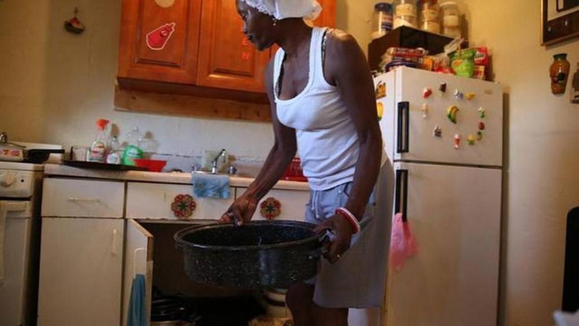 Seen in November 2014, Joyce McGill empties water from a leaky kitchen sink at 6040 NW 12th Ave. She tosses out the water from the roast pan into her bathroom toilet.