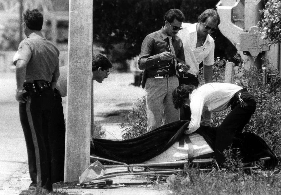 The body of Carl Brown is raised unto a gurney, next to a pole he was crushed against after being shot by a friend of the victims inside nearby Bob Moore’s Welding and Machine Shop on North River Road.