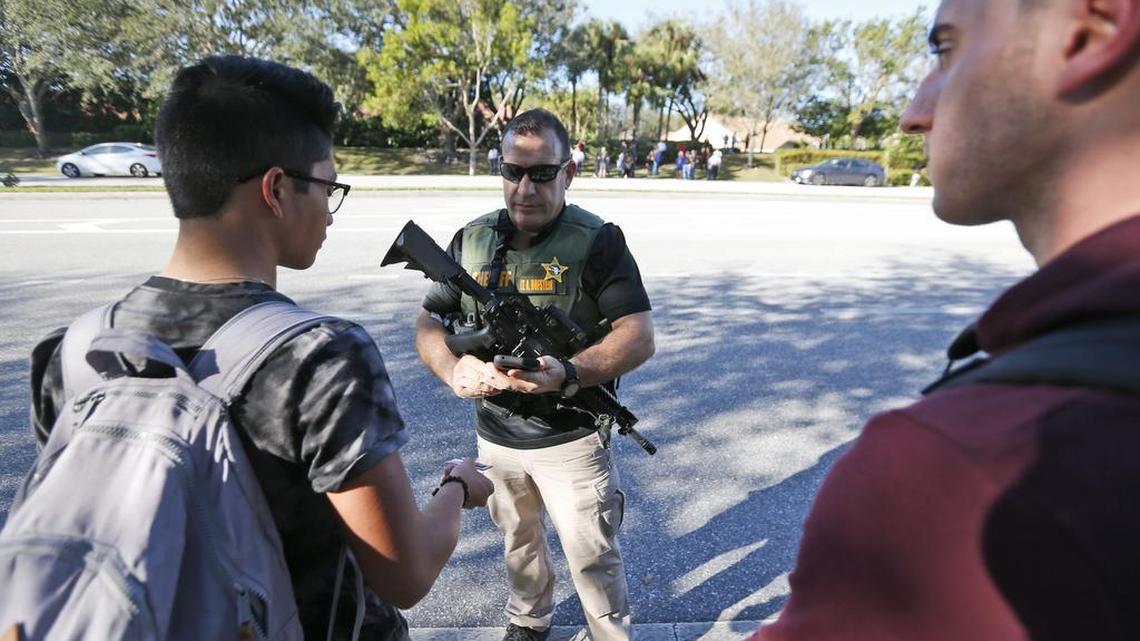 A law enforcement officer equipped with a rifle talks with students at Marjory Stoneman Douglas High School after a shooter killed 17 people on the campus on Feb. 14, 2018.