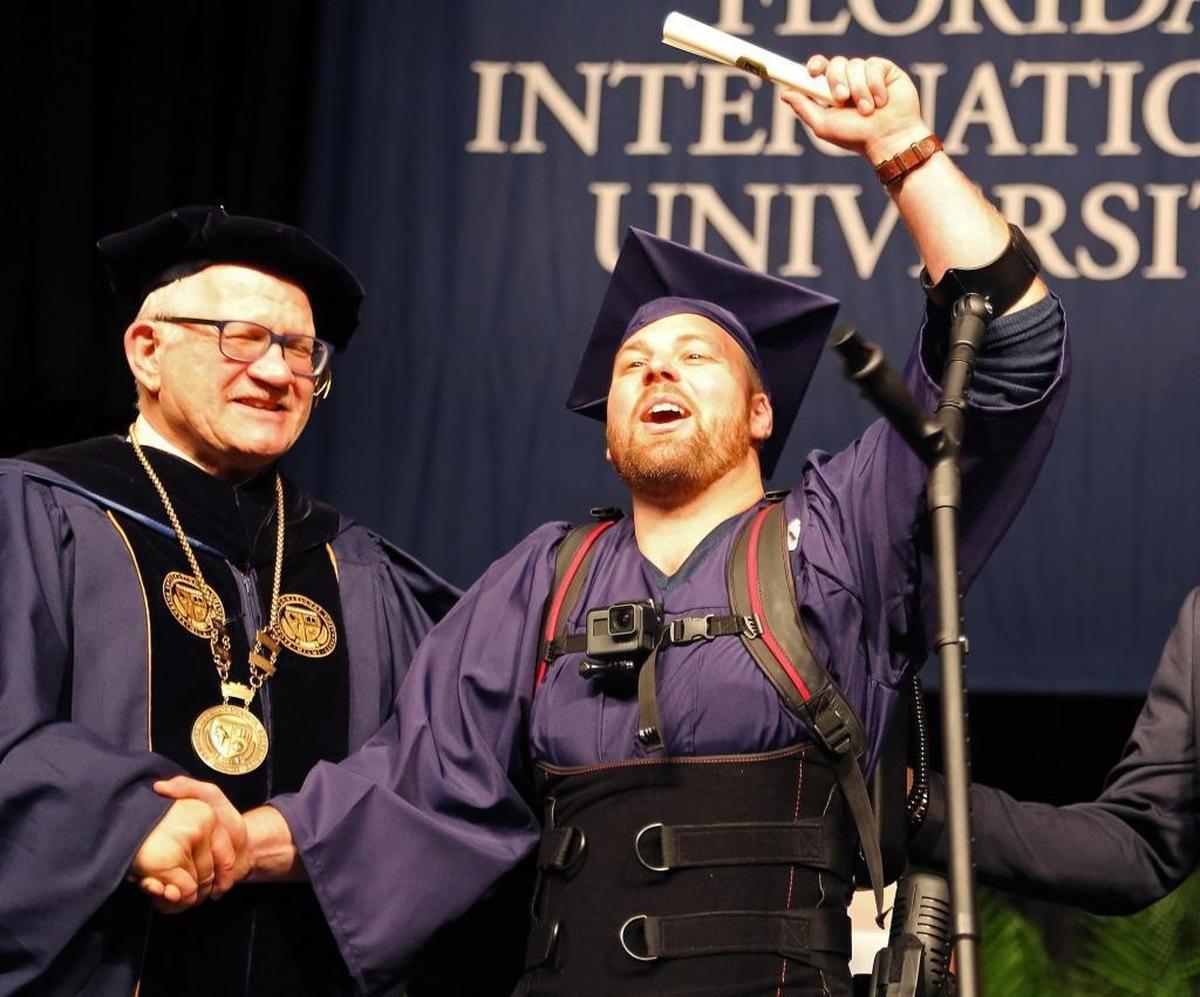 FIU graduate Shane Mosko lifts up his diploma as he shakes the hand of FIU President Mark Rosenberg. Mosko, who is paralyzed from the waist down, walked across the stage to receive his diploma while wearing an exoskeleton device on Sunday, Dec. 17, 2017, at FIU’s commencement ceremony.