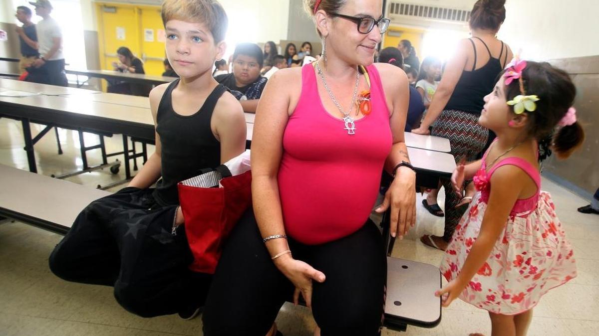 Mercedes Cabrera, center, who is eight months pregnant, waits with her children Emanuel, 12, left, and Rosalinda, nearly 5, to get free school uniforms on Thursday at Eneida M. Hartner Elementary School in Miami.