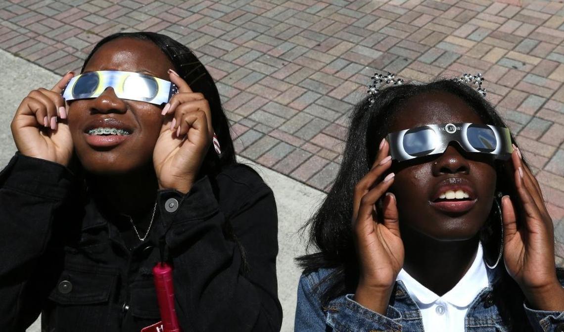 On the first day of school, eleventh grade students and sisters Stephanie Byrd, 16, and Danyel Rolle, 15, right, gaze toward the sky to witness the partial eclipse at Booker T. Washington Senior High School on Monday, August 21, 2017.
