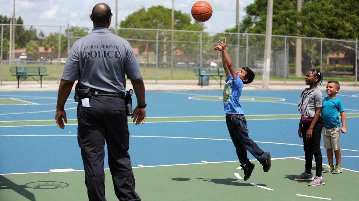 Coral Springs Police Officer Brian Gasper, a school resource officer at Coral Springs Charter School, watches as Summer BreakSpot camper, Jayden Boodram, takes a basketball shot on July 19, 2016.