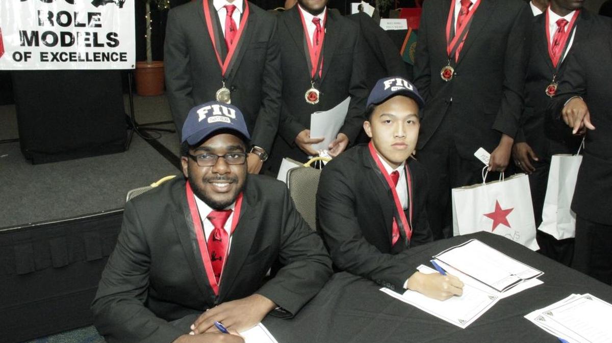 Students from 5000 Role Models of Excellence pose as they sign the paperwork for their college scholarships.