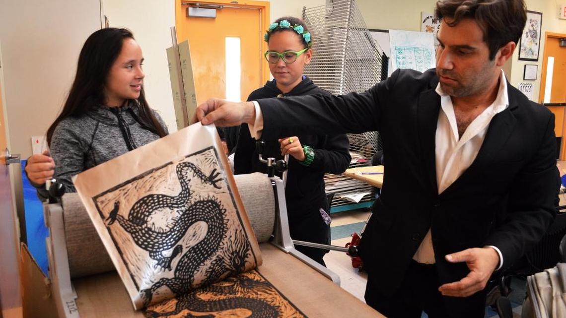 Brian Reedy, right, reveals a print produced by students Katiana Rodriguez, center, and Pamela Cianciarullo, left.