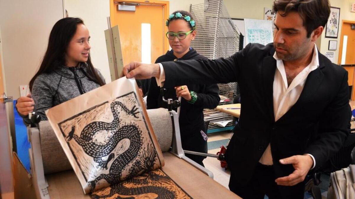 Brian Reedy, right, reveals a print produced by students Katiana Rodriguez, center, and Pamela Cianciarullo, left.