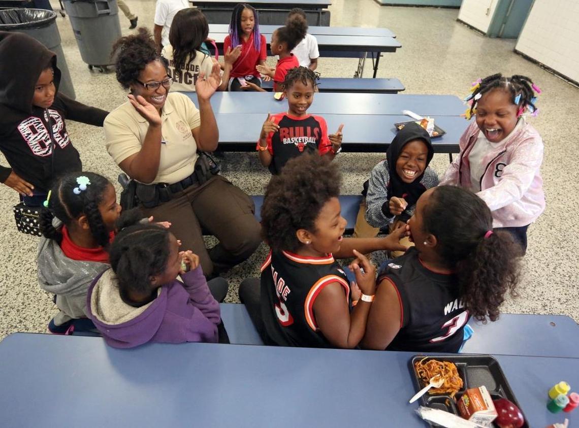Miami-Dade police officer, Camille Normil, laughs along with a group of third graders following a patty-cake game they were playing during lunchtime at Poinciana Park Elementary School, Tuesday morning, May 16, 2017. Once a month, the Miami-Dade Police Department sends officers to the school to have lunch with students. When the program first started, the children were wary of the officers because they were used to seeing police in the area only when there was trouble. The kids now look at the officers as friends.