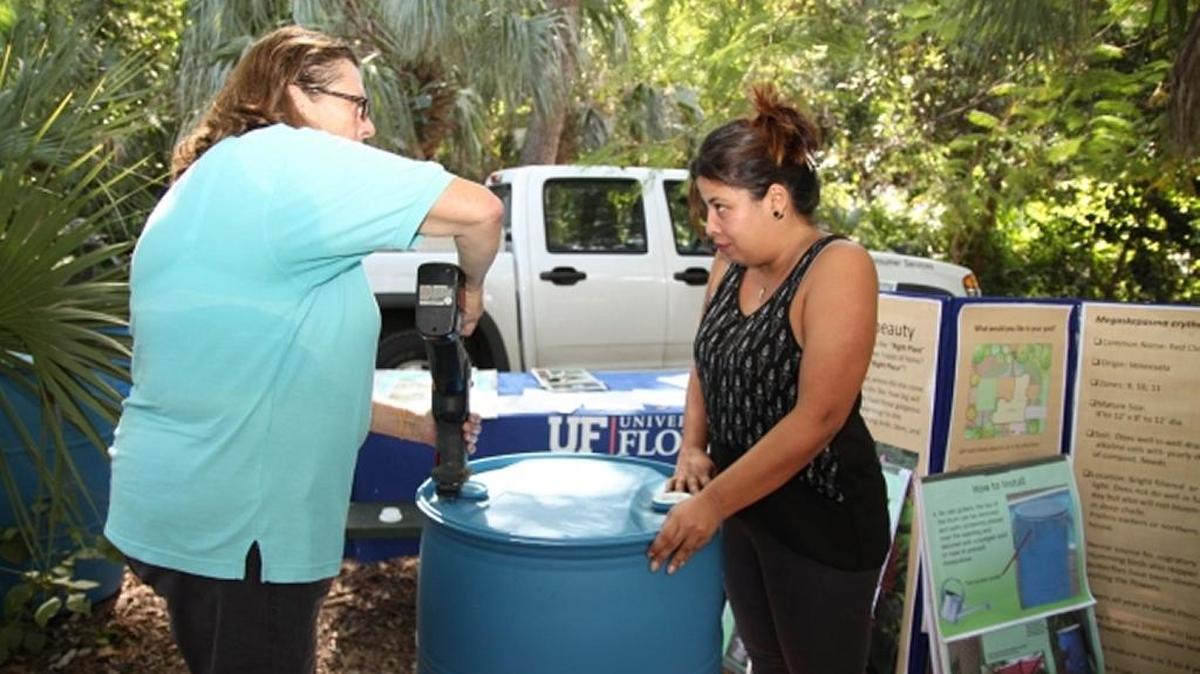 Barbara McAdam, with Florida Yards and Neighborhoods Program, cuts the top off a rain barrel as Sandra Arizmendi, a Miami artist, grips the side.