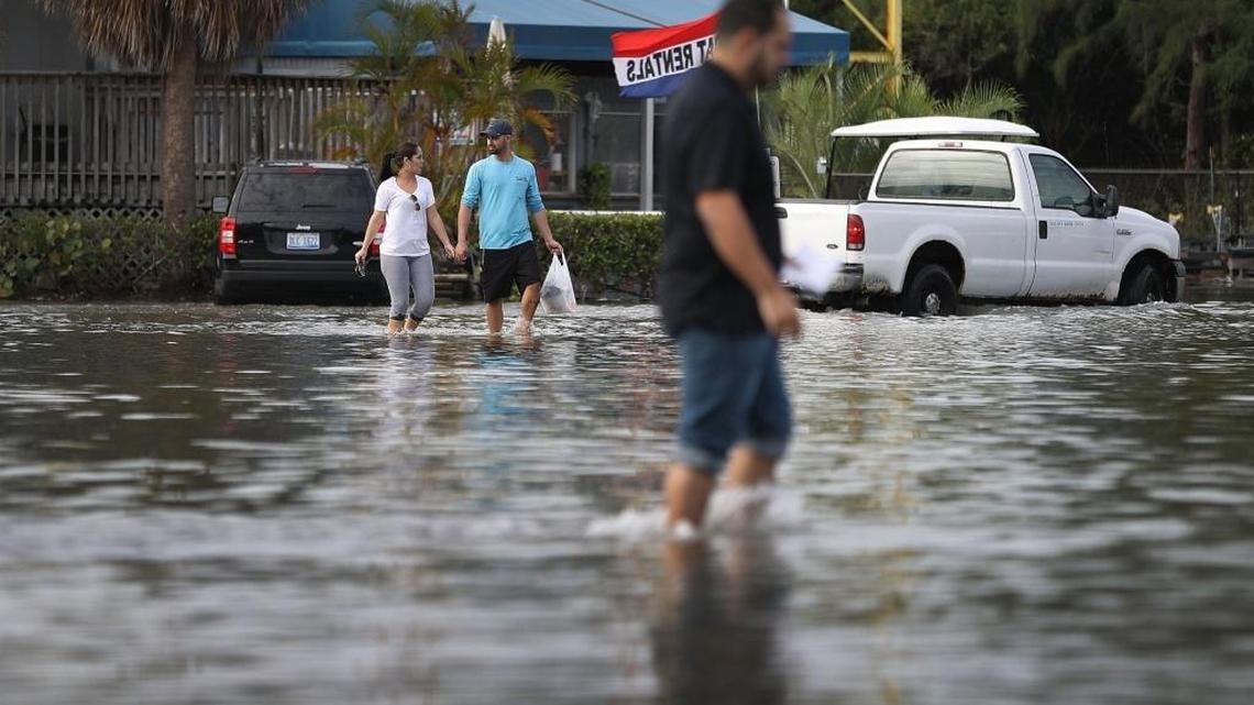 Yaneisy Duenas (left) and Ferando Sanudo walk through a flooded parking lot at the Haulover Marine Center during a king tide in November. Florida scientists on Monday sent President Donal Trump warning that cuts to NOAA’s polar satellite network could hurt research on climate change.