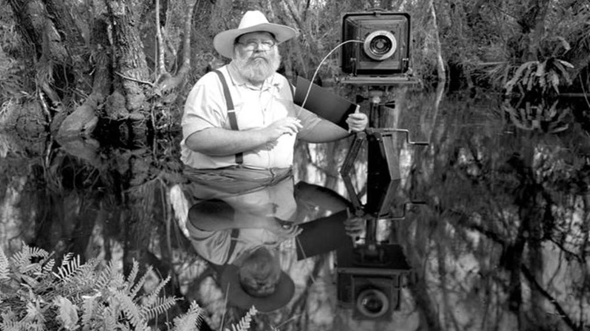 Clyde Butcher standing in the Florida Everglades with his large-format camera by his side.