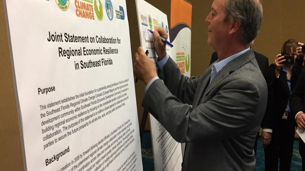 Broward County Mayor Beam Furr symbolically signs the Southeast Florida Climate Compact agreement on Thursday, Dec. 14 to collaborate with the business community of the region to research, lobby for and enact solutions to climate change.