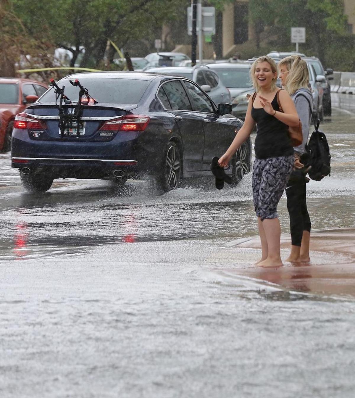 Pedestrians carry their shoes in their hands as they try to cross a flooded Collins Ave. and 24th Street on Thursday.