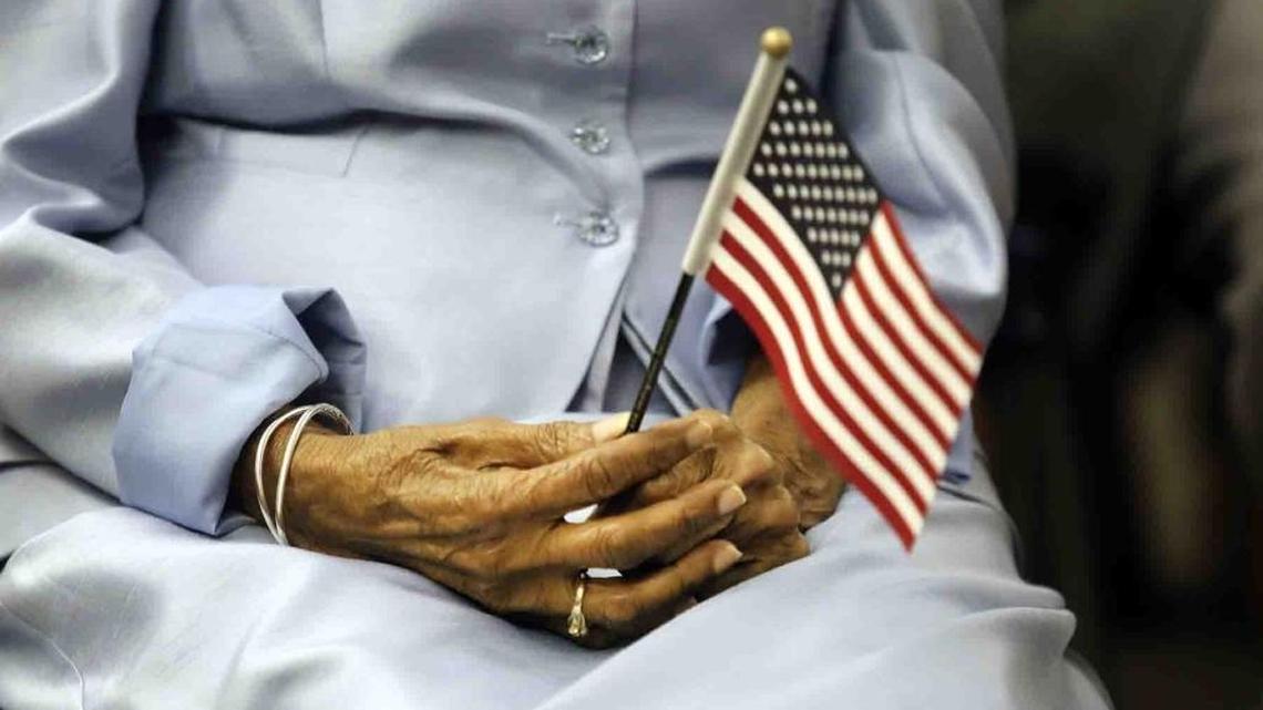 A woman holds a small United States flag during a ceremony to be sworn in as a United States citizen.
