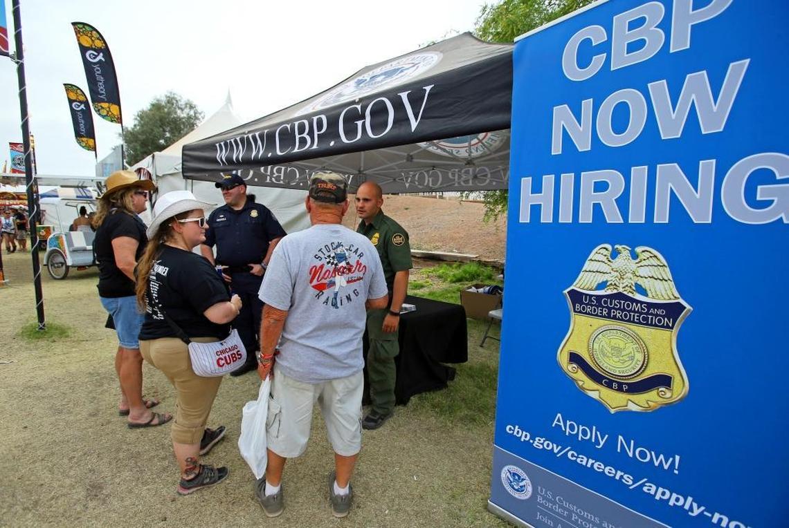 In this April 9, 2017, photo, U.S. Border Patrol agents talk to visitors at a recruitment tent set up at the Country Thunder Music Festival in Florence, Ariz.