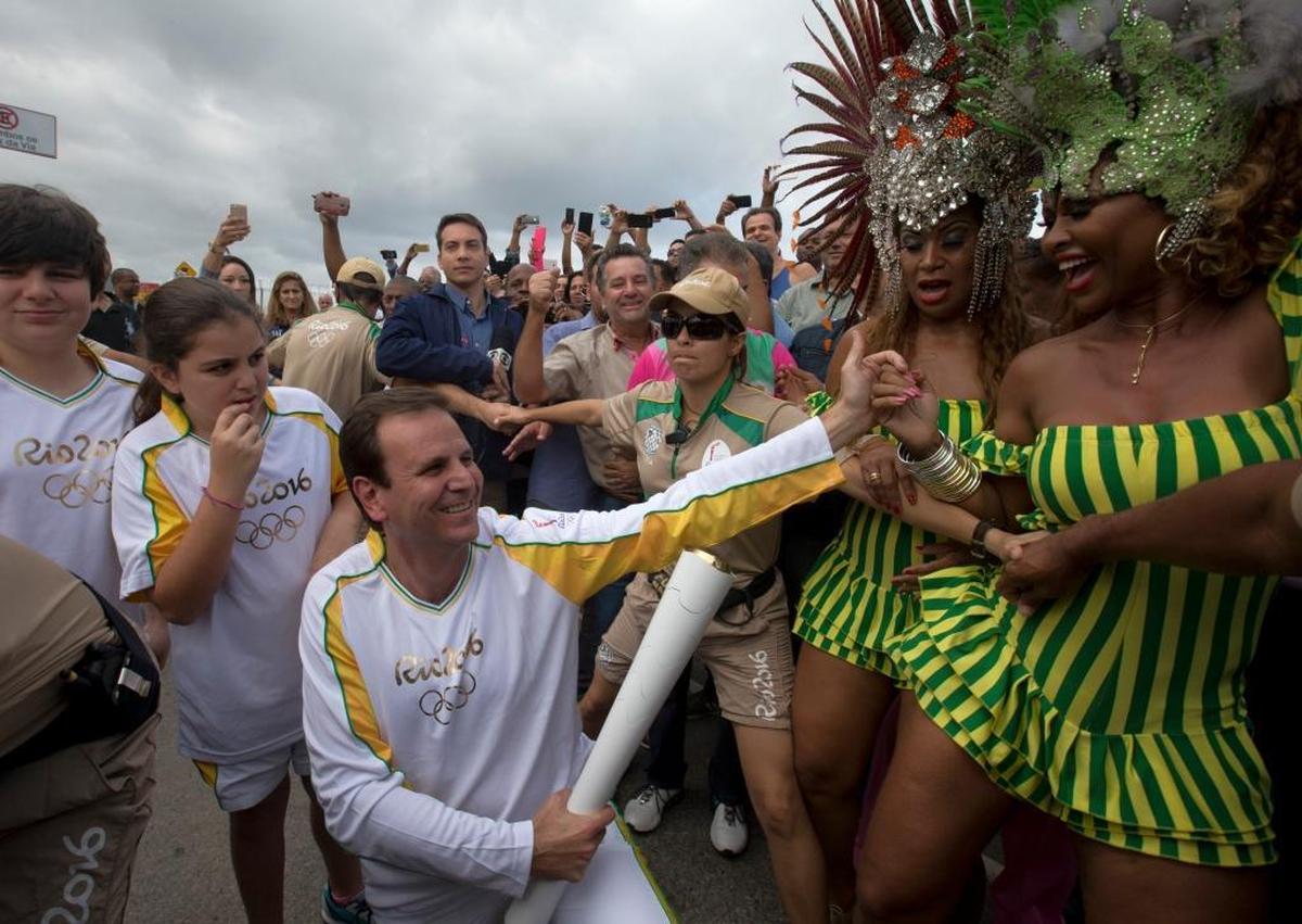 Then-Rio de Janeiro Mayor Eduardo Paes, center, holds the Olympic torch during Rio’s Olympics festivities in 2016. Rio was the first South American city granted the honor of hosting the Olympic games, but several officials, including Paes, have since been suspected of coordinating bribes to sway the Olympic committee. (AP Photo/Silvia Izquierdo)