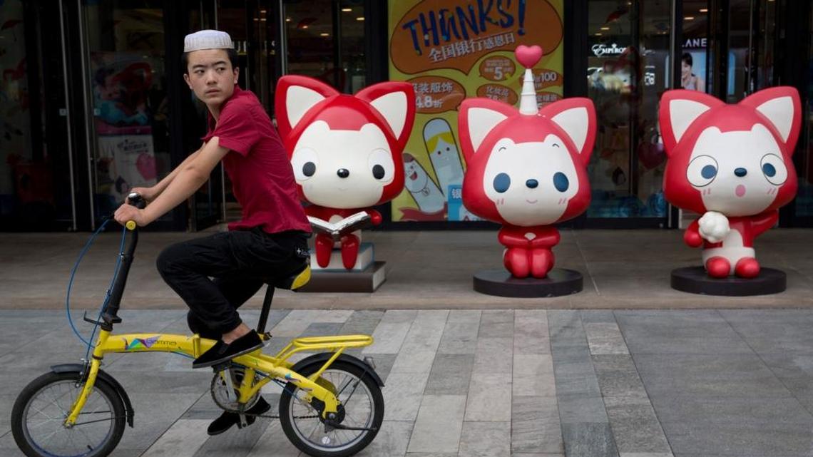 A man wearing an ethnic minority cap rides past cartoon mascots outside a shopping mall in Beijing, China, Wednesday, Aug. 17, 2016. The United Nations' intellectual property organization says Monday, Aug 15, 2016 that China has joined the world's top 25 most innovative economies for the first time.