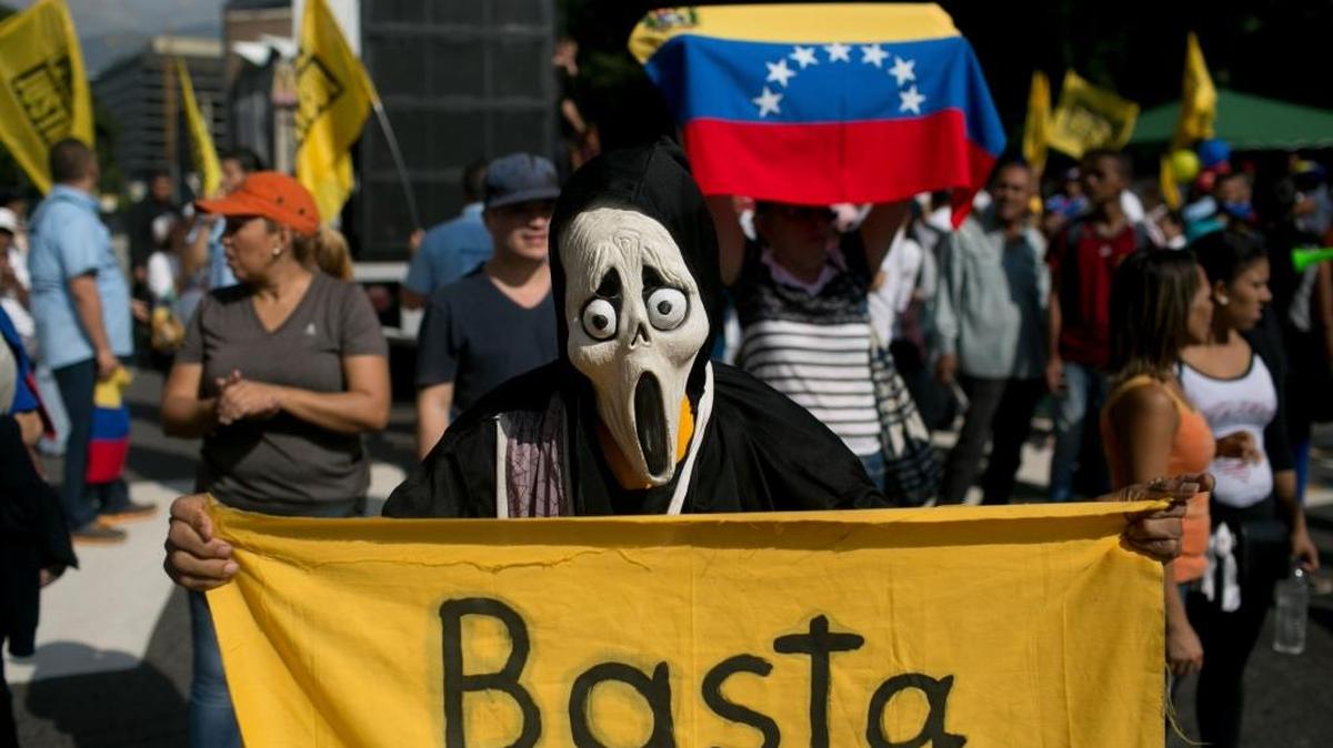 A protester, wearing a Ghostface mask and holding a banner that reads in Spanish, "Enough," takes part in a protest against President Nicolás Maduro, in Caracas, Venezuela Wednesday.