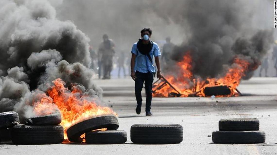 A masked protester walks between burning barricades in Managua, Nicaragua, in April. Protesters opposed to social security reforms faced off against riot police and pro-government groups.