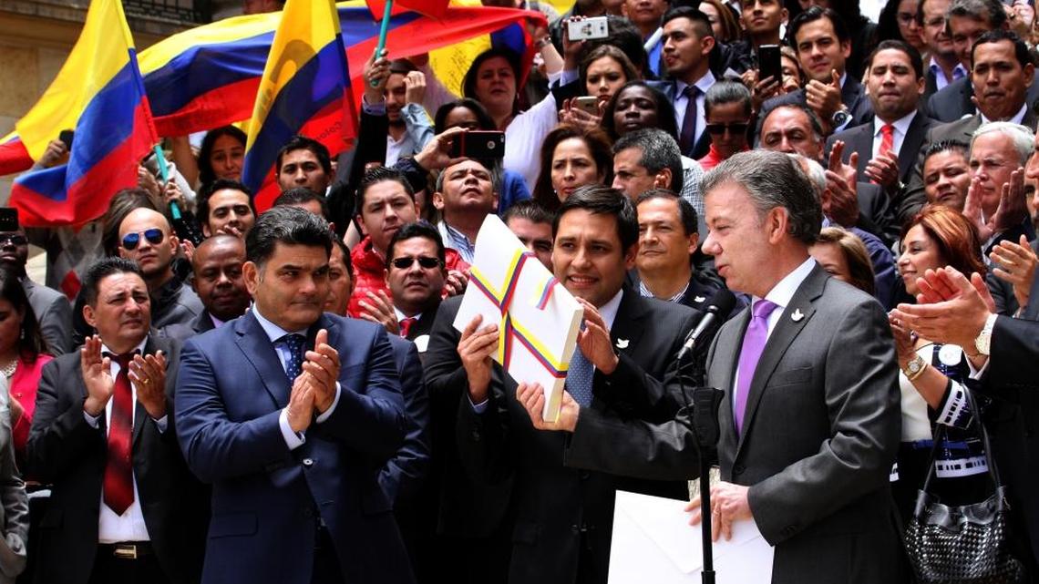 The leader of Colombia’s Senate, Mauricio Lizcano, receives from Colombia’s President Juan Manuel Santos, right, the peace deal with FARC rebels on Aug. 25.