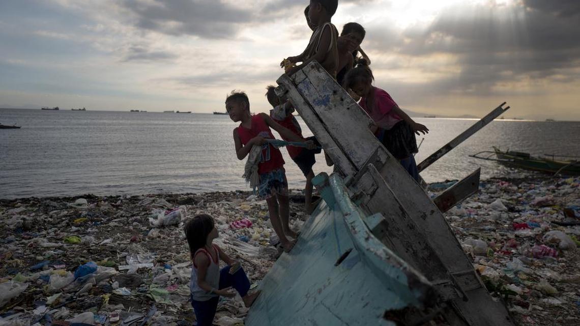 Children in the Philippines play on a beach littered with plastic trash washed up on shore.